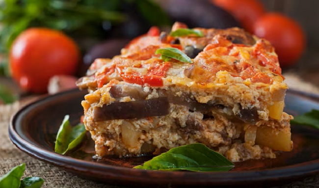 Moussaka on a plate with tomatoes in the background.